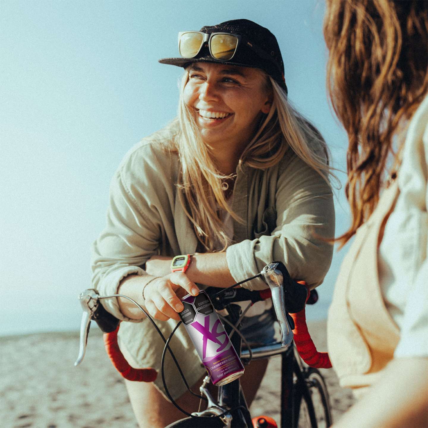 Dos mujeres, una de ellas en bicicleta y en la mano una lata de XS Cranberry Grape